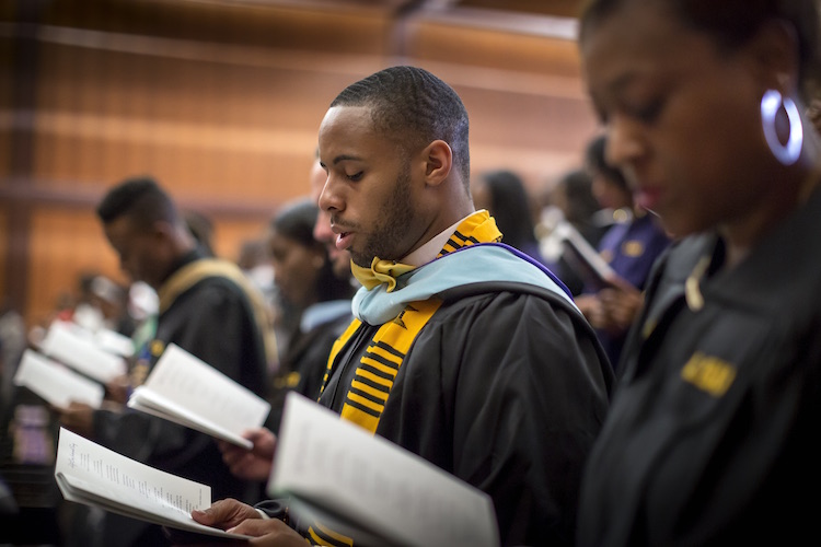 Student reads aloud in graduation regalia. 